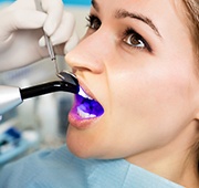 A curing light being used on a female patient’s teeth during porcelain veneer placement