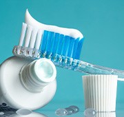 Toothbrush on tub of toothpaste on reflective surface with water droplets