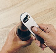 Hands using bottle opener to pry off bottle cap
