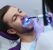 Dentist applying UV light to man’s dental bonding