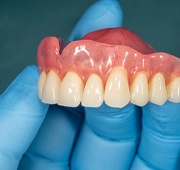 A person wearing a medical glove and holding a full top denture for a patient