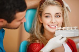 a dentist using a shade guide on a young woman’s smile