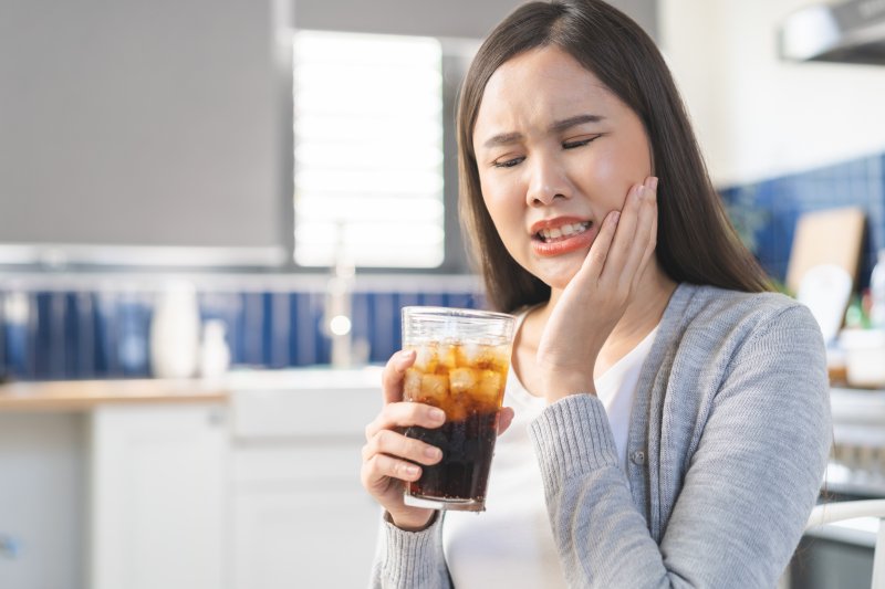 young woman experiencing tooth sensitivity while drinking a soda